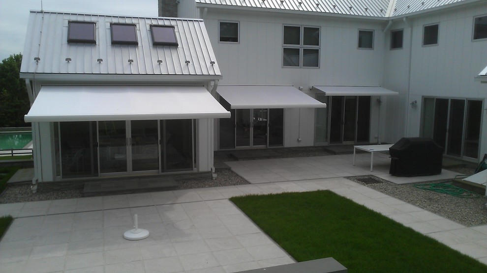 Photo of a medium sized contemporary back patio in New York with natural stone paving and an awning.