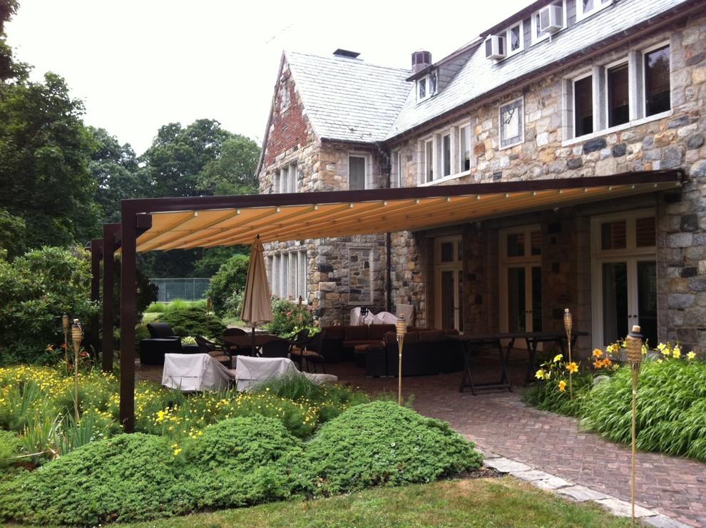 Foto di un ampio patio o portico tradizionale dietro casa con pavimentazioni in mattoni e un parasole