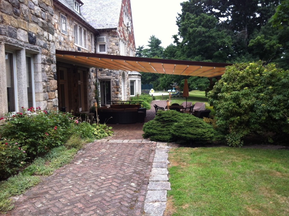 Idée de décoration pour une très grande terrasse arrière tradition avec des pavés en brique et un auvent.