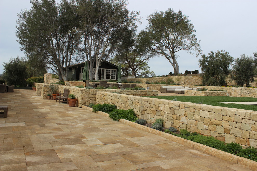 This is an example of an expansive mediterranean back patio in Los Angeles with a water feature, natural stone paving and no cover.