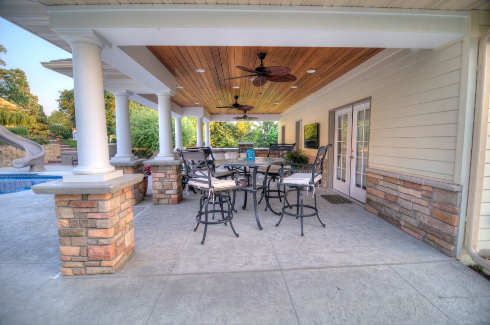 This is an example of a large traditional back patio in Cedar Rapids with a fire feature, stamped concrete and a roof extension.