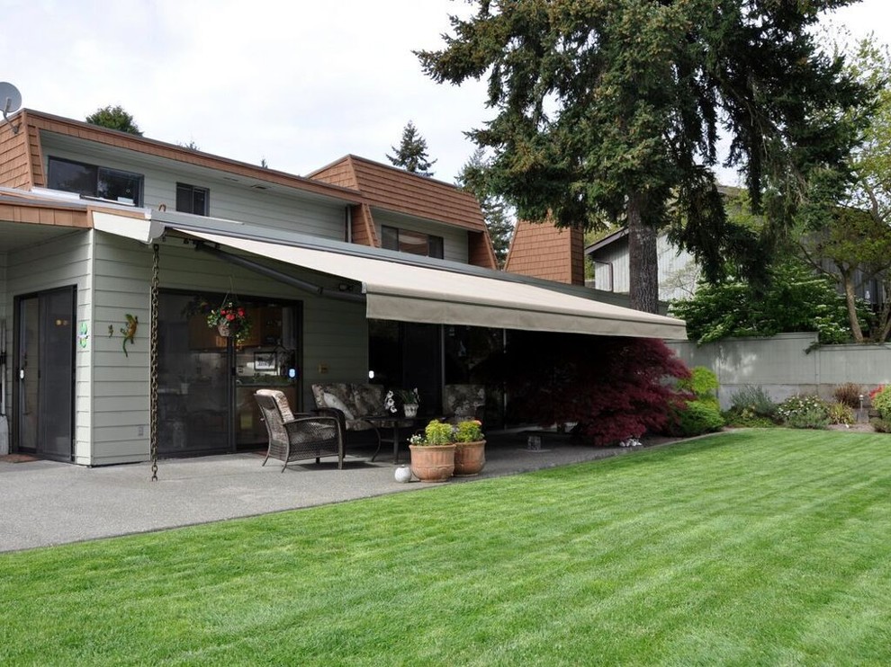Пример оригинального дизайна: большой двор на заднем дворе в стиле ретро с покрытием из бетонных плит и козырьком