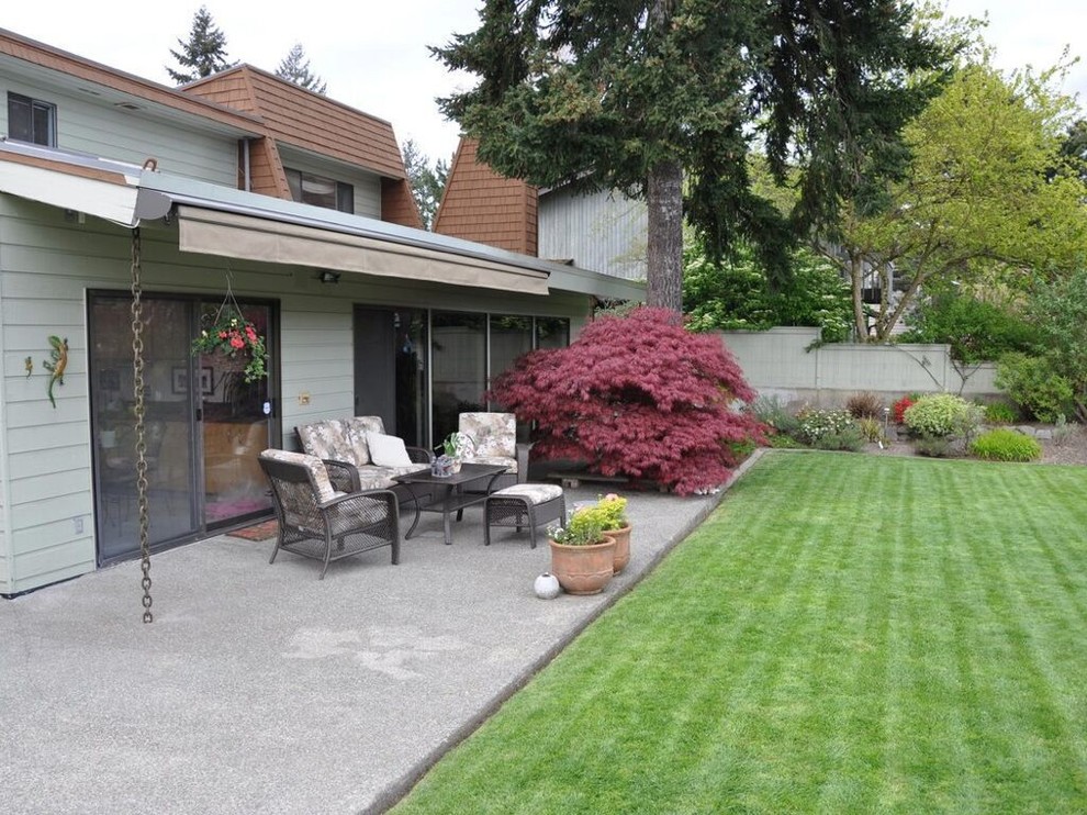 Cette image montre une grande terrasse arrière vintage avec une dalle de béton et un auvent.