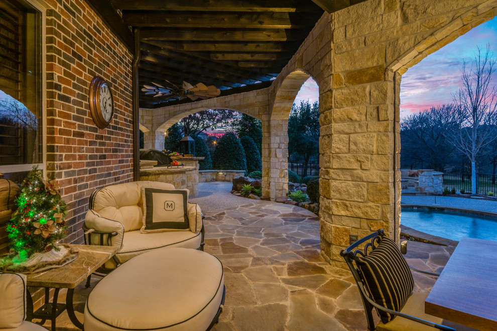 Aménagement d'une grande terrasse arrière montagne avec une cuisine d'été, des pavés en pierre naturelle et une pergola.