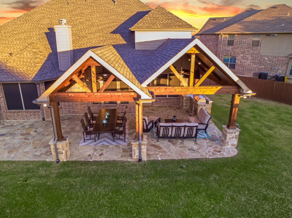 This is an example of a medium sized rural back patio in Dallas with an outdoor kitchen, natural stone paving and a roof extension.