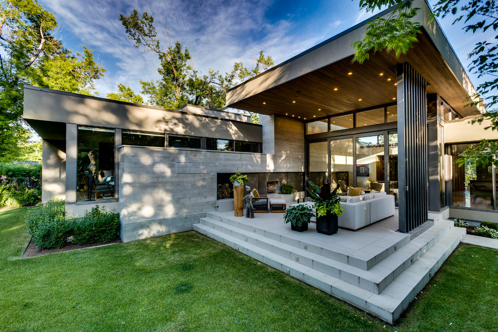 Réalisation d'une grande terrasse arrière minimaliste avec une extension de toiture, un foyer extérieur et des pavés en béton.