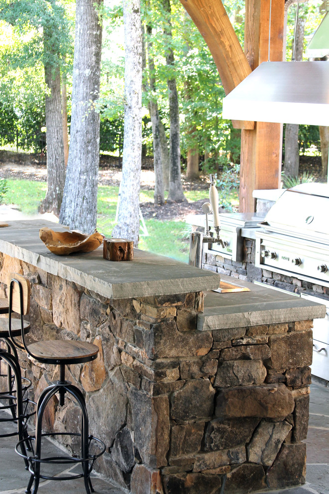 Aménagement d'une grande terrasse arrière classique avec une cuisine d'été, des pavés en pierre naturelle et une extension de toiture.