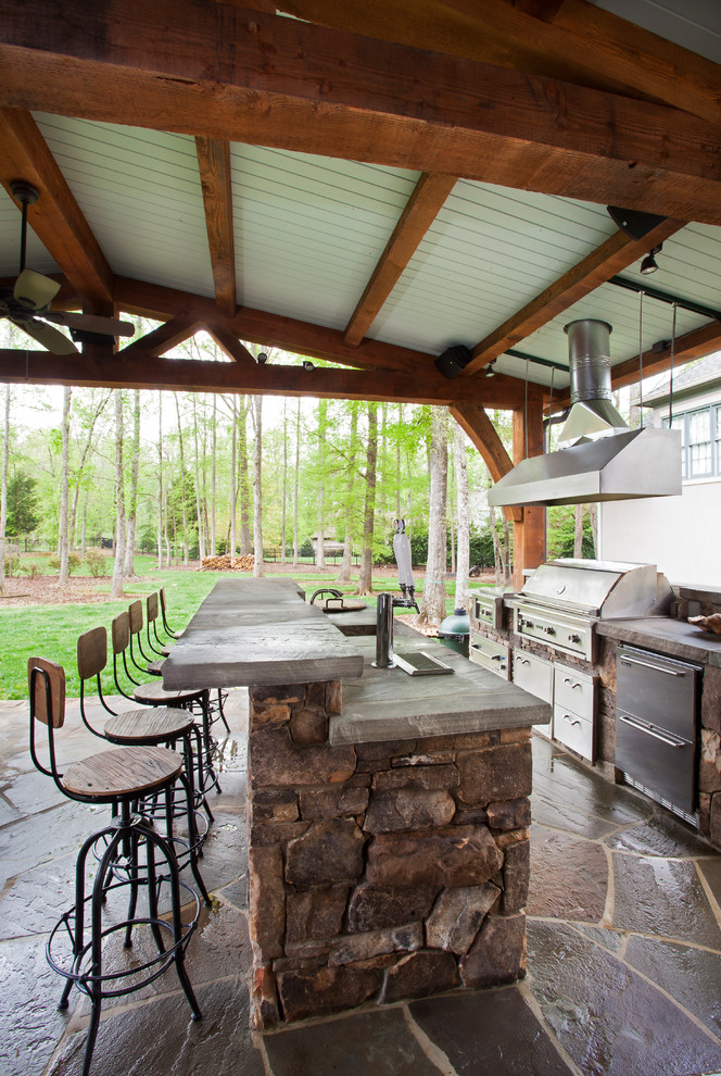 Aménagement d'une grande terrasse arrière classique avec une cuisine d'été, des pavés en pierre naturelle et une extension de toiture.