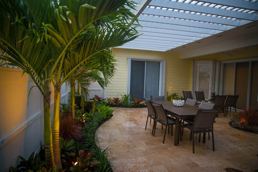 Small world-inspired courtyard patio in Miami with a water feature, natural stone paving and a pergola.