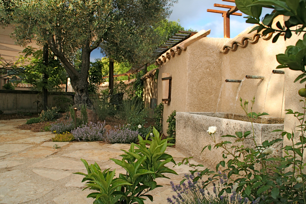 Diseño de patio mediterráneo sin cubierta con fuente y adoquines de piedra natural