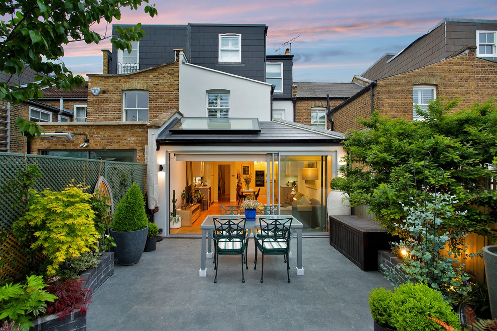 This is an example of a medium sized contemporary back patio in London with a potted garden, natural stone paving and no cover.