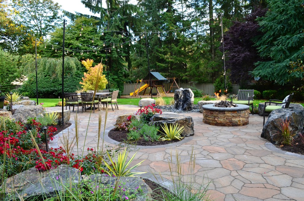 This is an example of a large traditional back patio in Seattle with a fire feature, natural stone paving and no cover.