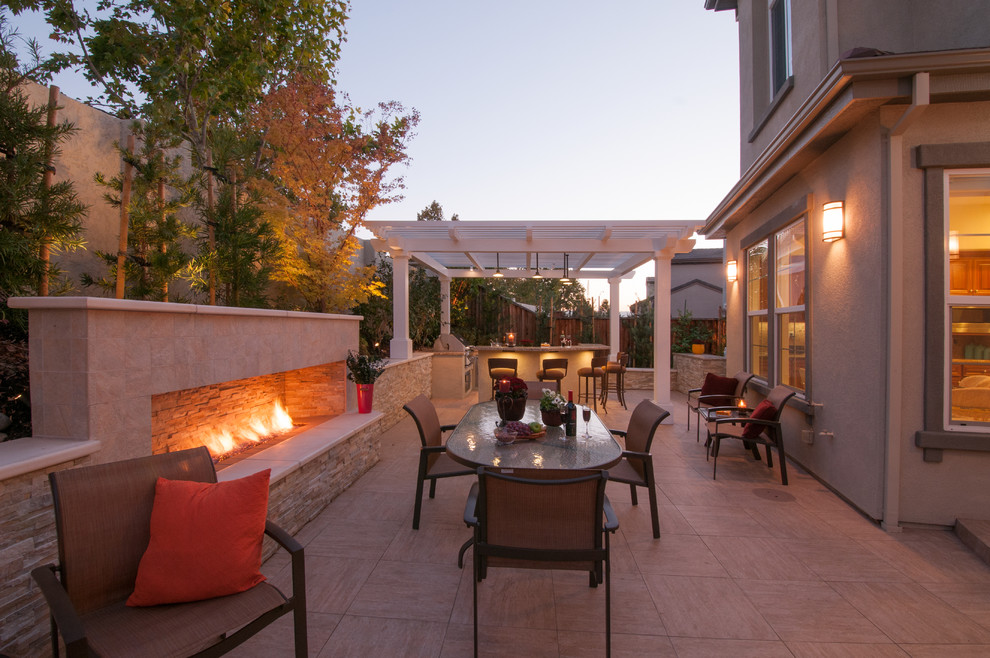 Exemple d'une grande terrasse arrière tendance avec une cuisine d'été, du carrelage et une pergola.
