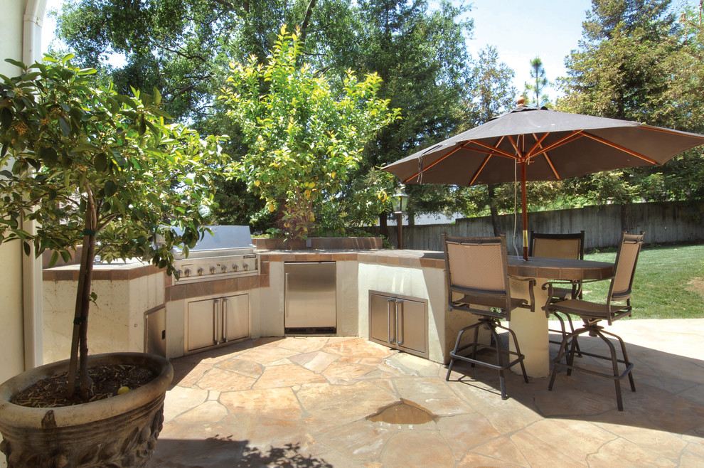 Aménagement d'une grande terrasse arrière classique avec une cuisine d'été, des pavés en pierre naturelle et aucune couverture.