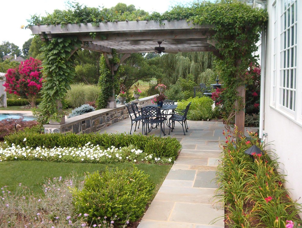 Photo of a large rural back patio in Philadelphia with natural stone paving and a pergola.