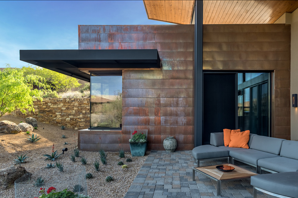 Réalisation d'une grande terrasse arrière minimaliste avec une cuisine d'été, des pavés en brique et une extension de toiture.