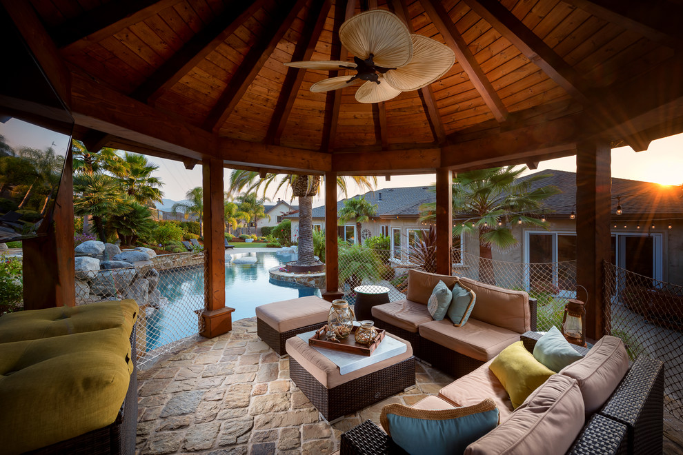 Idee per un patio o portico tropicale dietro casa con pavimentazioni in pietra naturale e un gazebo o capanno