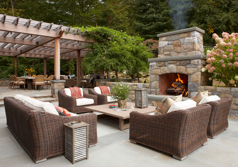 This is an example of a rural back patio in New York with a fireplace, natural stone paving and no cover.
