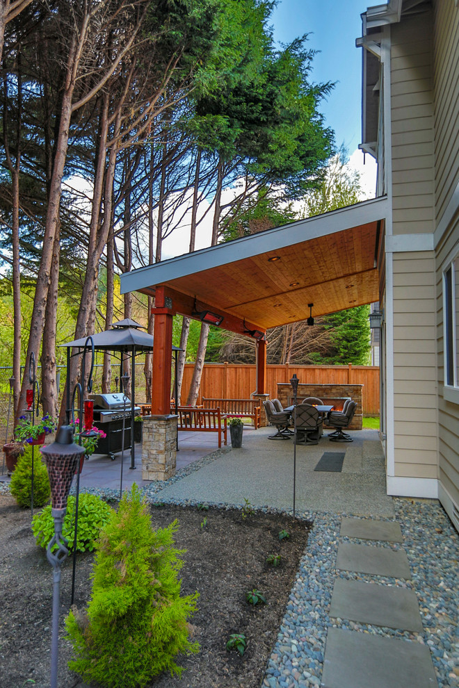 Immagine di un patio o portico american style di medie dimensioni e dietro casa con un caminetto, pavimentazioni in cemento e un tetto a sbalzo