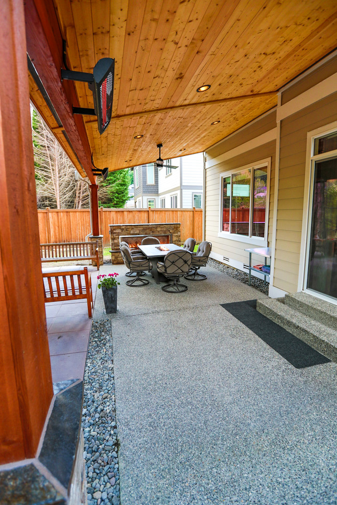 Immagine di un patio o portico stile americano di medie dimensioni e dietro casa con un caminetto, pavimentazioni in cemento e un tetto a sbalzo