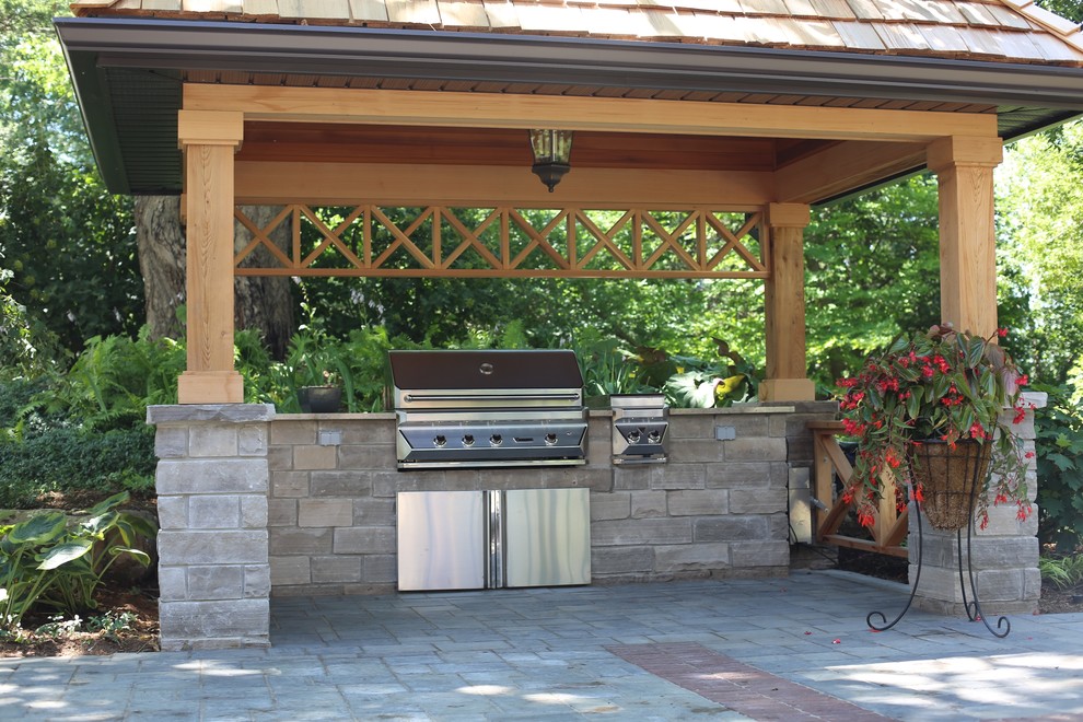 Cette photo montre une grande terrasse arrière chic avec une cuisine d'été, des pavés en béton et un gazebo ou pavillon.