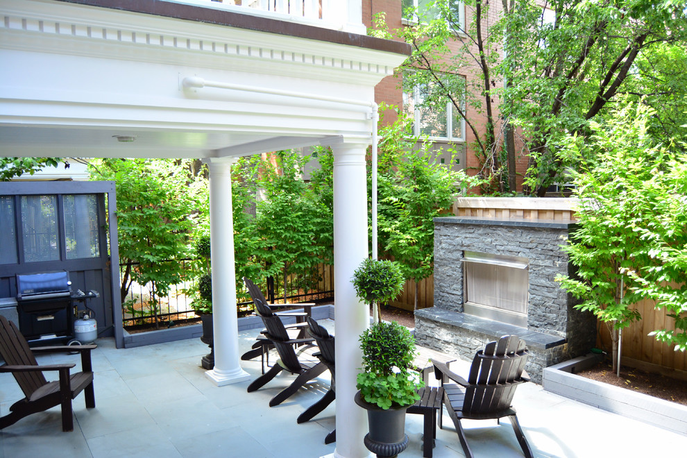 Réalisation d'une grande terrasse arrière tradition avec un foyer extérieur, des pavés en béton et une extension de toiture.