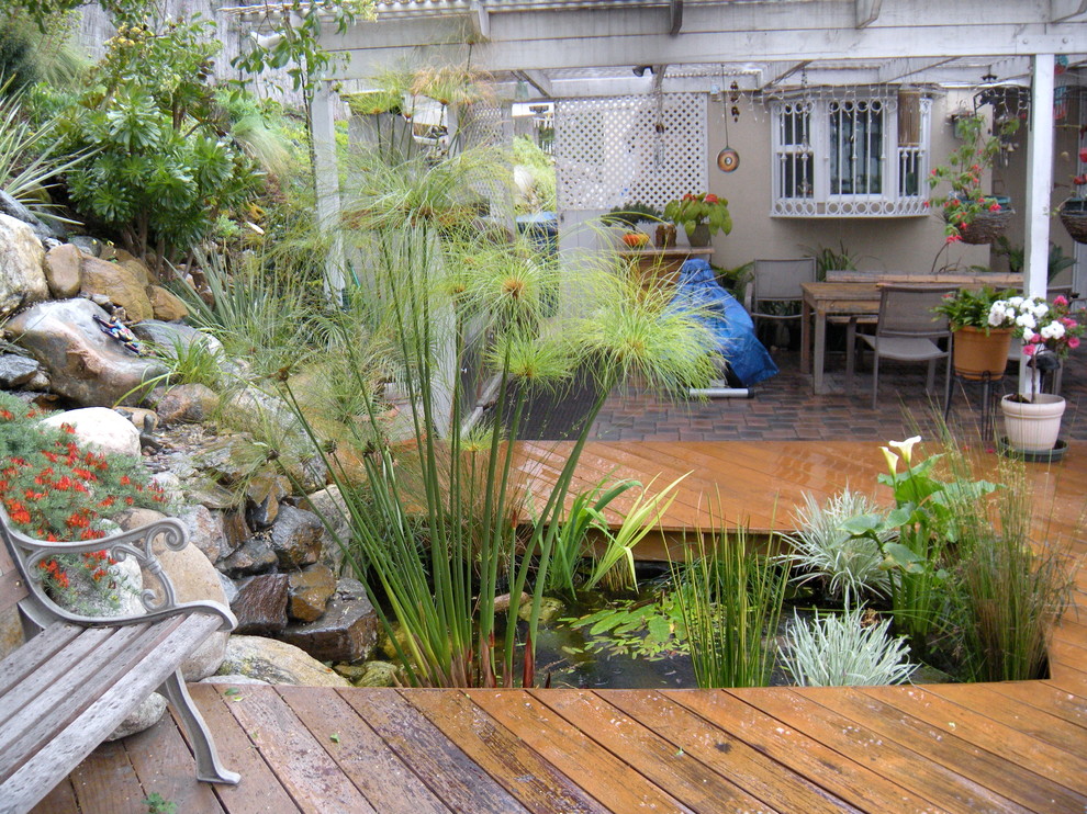 Cette photo montre une terrasse en bois arrière éclectique de taille moyenne avec une pergola et un point d'eau.