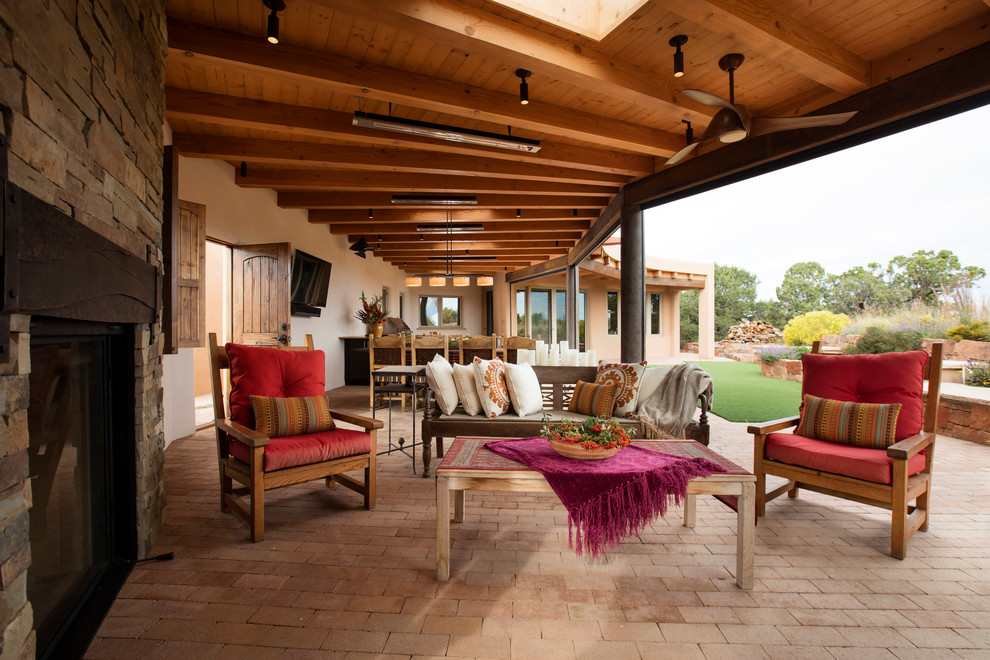 Immagine di un grande patio o portico contemporaneo dietro casa con un caminetto, pavimentazioni in mattoni e un tetto a sbalzo