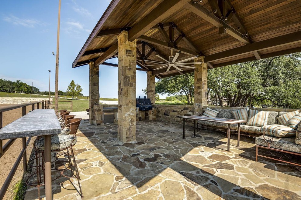 Photo of a large rustic back patio in Austin with an outdoor kitchen, natural stone paving and a roof extension.