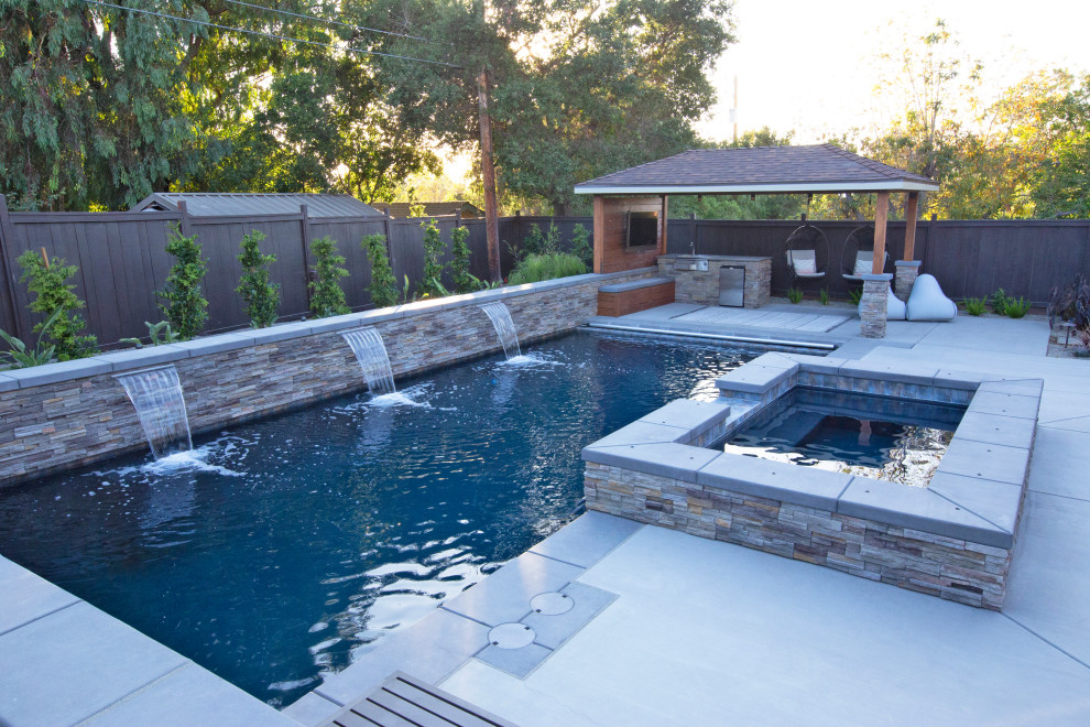 Modelo de piscina con fuente minimalista grande en patio trasero con losas de hormigón