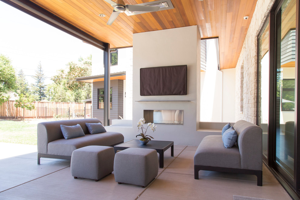 Idée de décoration pour une terrasse arrière design de taille moyenne avec un foyer extérieur, une dalle de béton et une extension de toiture.