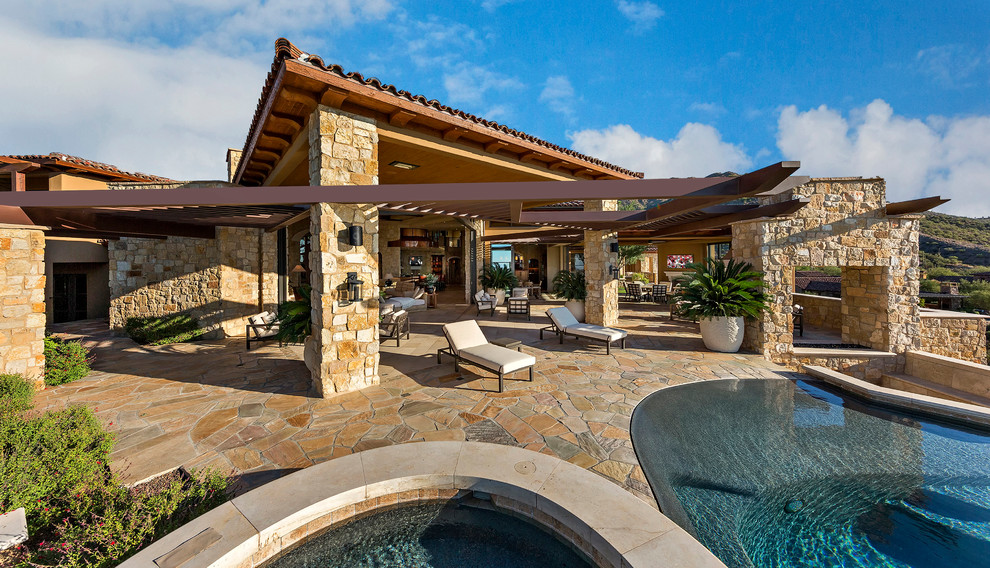 This is an example of an expansive contemporary back patio in Phoenix with a fire feature, natural stone paving and a pergola.