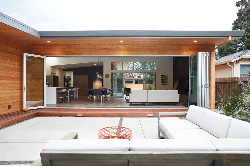 Cette image montre une terrasse arrière vintage de taille moyenne avec un foyer extérieur, une dalle de béton et une extension de toiture.