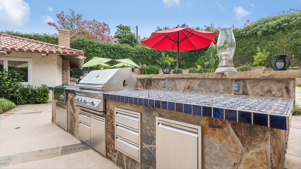 Patio kitchen - large transitional backyard stone patio kitchen idea in Orange County with a pergola
