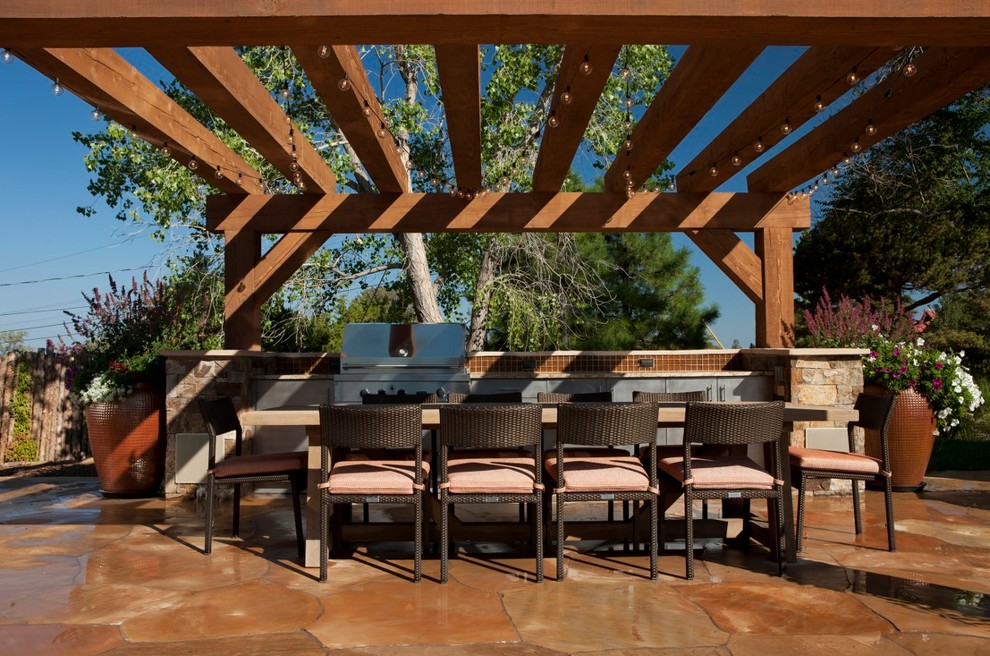 Cette image montre une grande terrasse arrière chalet avec une cuisine d'été, des pavés en pierre naturelle et une pergola.