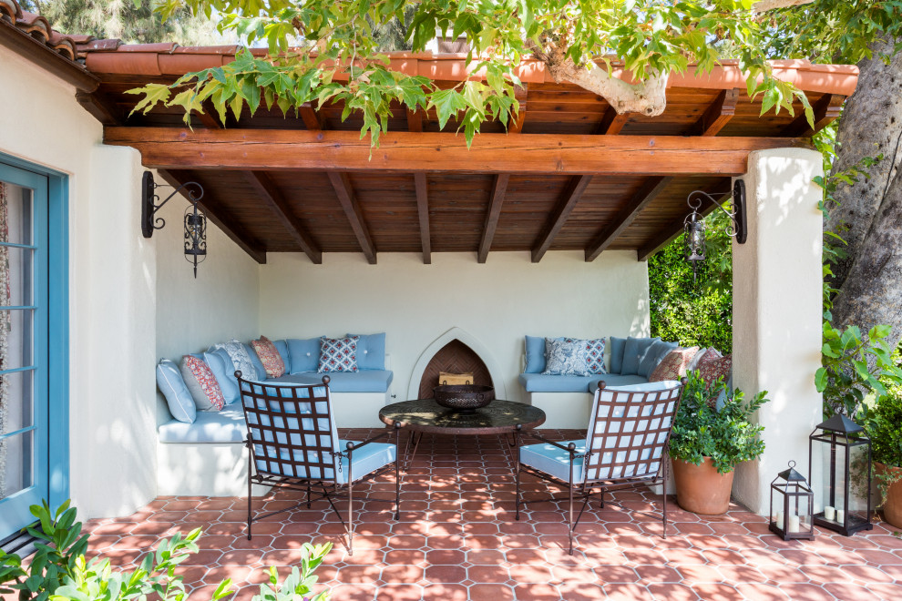 Foto di un patio o portico mediterraneo di medie dimensioni e dietro casa con un caminetto, piastrelle e un tetto a sbalzo