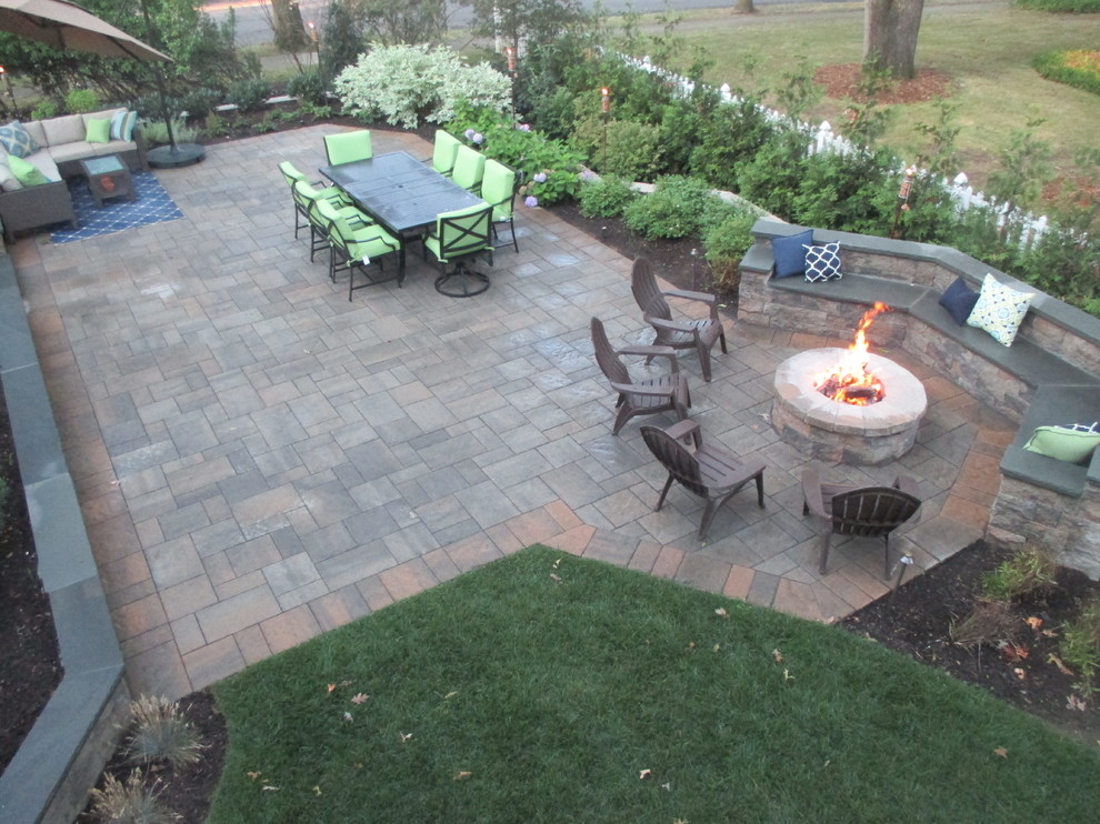 This is an example of a large classic back patio in New York with a fire feature, natural stone paving and no cover.