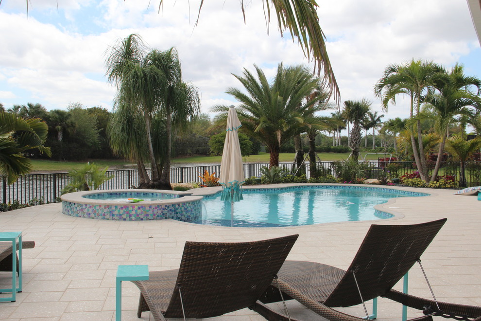 This is an example of a large world-inspired back swimming pool in Miami with natural stone paving.