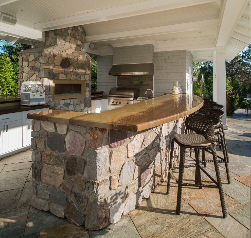 Réalisation d'une grande terrasse arrière tradition avec une cuisine d'été, des pavés en pierre naturelle et une pergola.