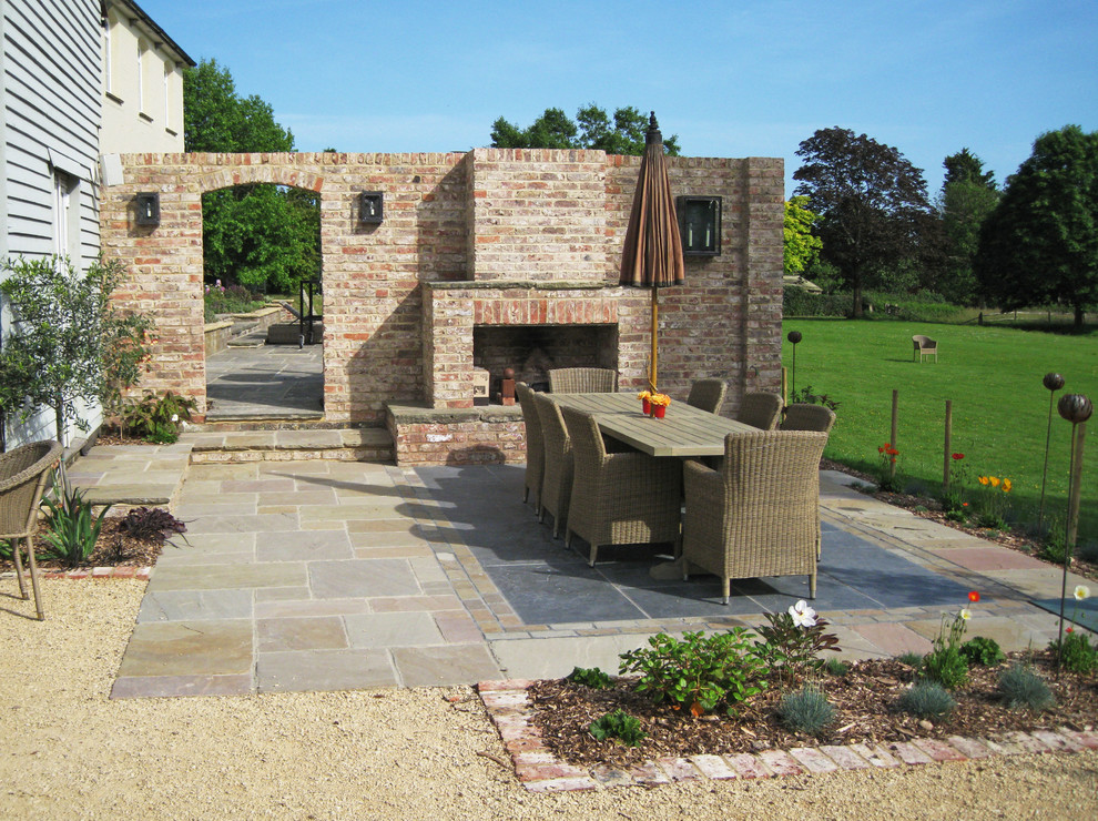 This is an example of a classic back patio in Sussex with no cover, natural stone paving and a fireplace.