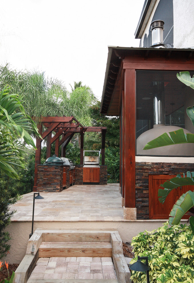 Foto di un ampio patio o portico tropicale dietro casa con pavimentazioni in pietra naturale e una pergola
