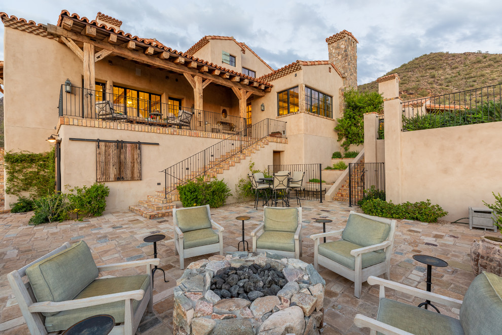 This is an example of a mediterranean back patio in Phoenix with a fire feature, natural stone paving and no cover.