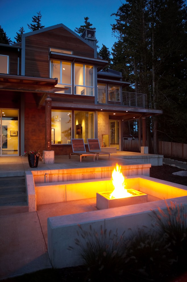 Cette image montre une terrasse avant minimaliste de taille moyenne avec un foyer extérieur, une dalle de béton et une extension de toiture.