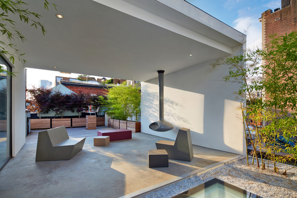 Cette photo montre une terrasse moderne de taille moyenne avec un foyer extérieur, une extension de toiture, une cour et une dalle de béton.