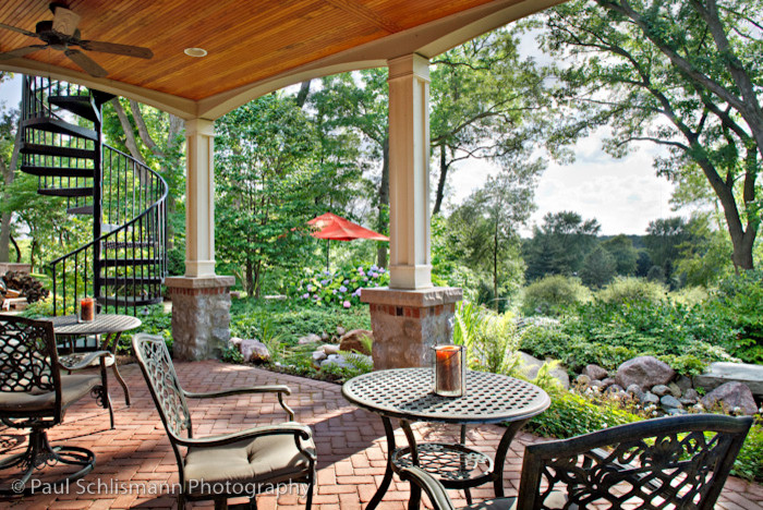 Immagine di un grande patio o portico tradizionale dietro casa con pavimentazioni in mattoni e un tetto a sbalzo
