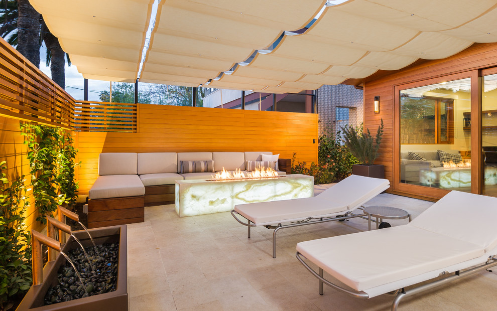 Photo of a medium sized contemporary patio in Los Angeles with a fire feature, tiled flooring and an awning.