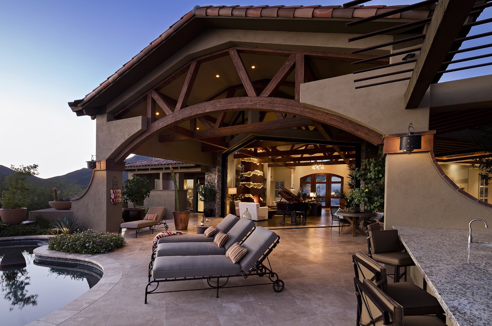 Réalisation d'une grande terrasse arrière sud-ouest américain avec une cuisine d'été, des pavés en pierre naturelle et une extension de toiture.