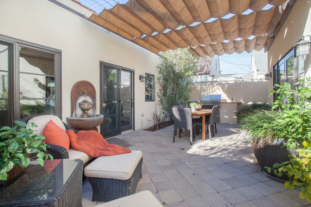 Modelo de patio mediterráneo de tamaño medio en patio trasero con cocina exterior, adoquines de piedra natural y toldo