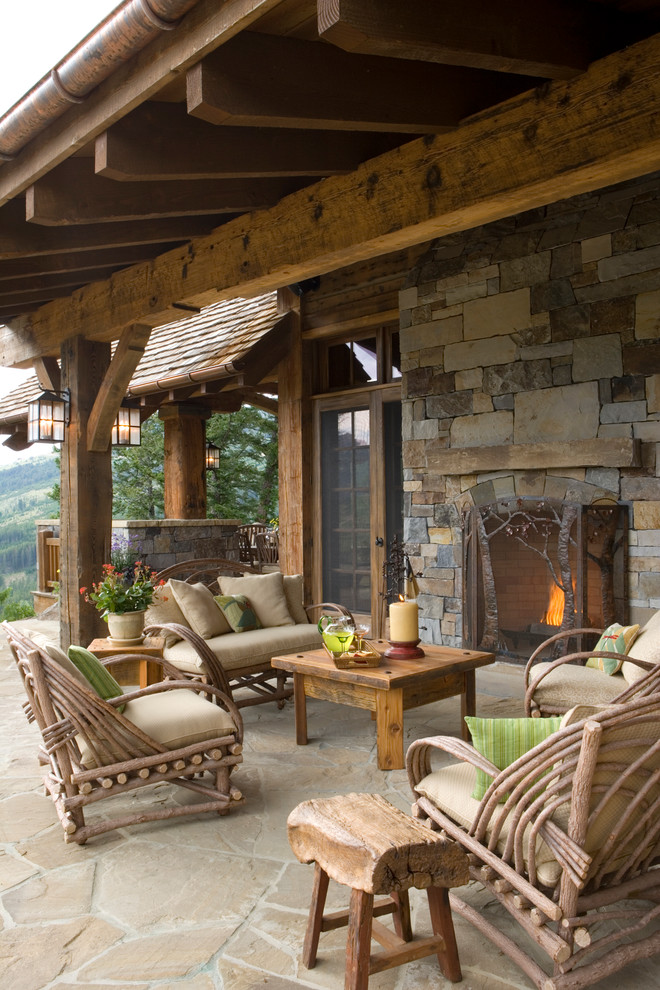 Réalisation d'une terrasse chalet avec un foyer extérieur, une extension de toiture et des pavés en pierre naturelle.