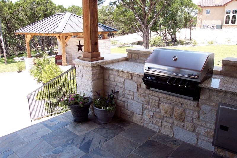 Modelo de patio de estilo americano de tamaño medio en patio trasero con cocina exterior, adoquines de piedra natural y cenador
